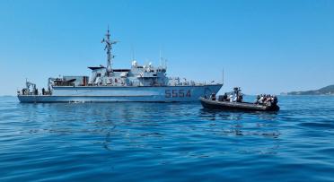 A naval ship and a tender operating together at sea on a calm, sunny day.. 